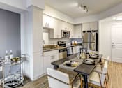 Thumbnail 6 of 18 - North Miami Beach, FL Luxury Apartments Near Aventura Mall - Lazul - Kitchen with Porcelain Wood-Style Plank Flooring, Stainless Steel Appliances, Quartz Countertops, White Cabinetry, and Dining Set.
