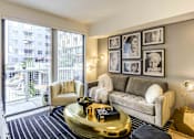Thumbnail 8 of 18 - Pet-Friendly Luxury Apartments in North Miami Beach, FL - Lazul - Living Room with Porcelain Wood-Style Plank Flooring, Area Rug, Couch, Armchair, Coffee Table, Side Table with Lamp, Standing Lamp, and Sliding Glass Door with Access to Balcony.