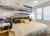 Thumbnail 10 of 18 - Luxury Apartments in North Miami Beach, FL with In-Unit Washer and Dryer - Lazul - Bedroom with Porcelain Wood-Style Plank Flooring, Plush Area Rug, Large Bed, Desk with Lamp, Wall Mural, and Large Window.