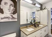 Thumbnail 11 of 18 - Luxury Apartments In North Miami Beach, FL, With An In-Unit Washer And Dryer - Lazul - Bathroom With Double-Sink Vanity, White Cabinetry, Large Mirror, Light Fixtures, And A Vase Of Flowers.