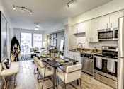 Thumbnail 7 of 18 - North Miami Beach, FL, Luxury Apartments Near Aventura Mall - Lazul - Kitchen With Soft-Close Cabinetry, Quartz Countertops, Stainless Steel Appliances, Dining Table, Chairs, And Cushioned Bench.