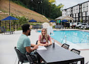 Thumbnail 17 of 32 - Two people sitting at a table by a pool.