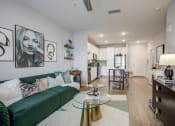Thumbnail 15 of 22 - Apartments for Rent in Downtown Greenville, SC - The Aster - Open Layout Living Room with Vinyl Plank Flooring, Area Rug, Sofa, Glass Coffee Table, Cabinet with Lamp, and View of Kitchen Area.