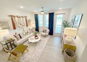Thumbnail 12 of 23 - A well-lit living room with a white sofa, a coffee table, and a rug.