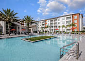 Thumbnail 2 of 27 - A large swimming pool in front of a multi-story apartment building.