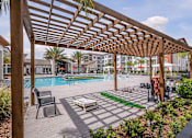 Thumbnail 11 of 27 - A wooden pergola over a poolside seating area.
