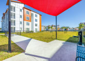 Thumbnail 16 of 23 - Two-Bedroom Apartments in Daytona Beach, FL - Madison Pointe - Leash-Free Dog Park with Lush Grass, Agility Course, and Bench Under Canopy.