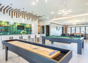Thumbnail 18 of 23 - One Bedroom Apartments in Daytona Beach, FL - Madison Pointe - Gaming Room with Billiards and Shuffleboard Tables, Pendant Lighting, Bar with Bar-Style Chairs, TV, and Lounge Seating