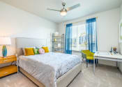 Thumbnail 8 of 23 - Pet-Friendly Apartments In Daytona Beach, FL - Madison Pointe - Bedroom With Bookshelf, Desk, Chair, Nightstand, Bed, Ceiling Fan, And Large Window.
