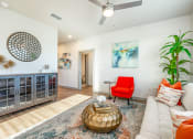 Thumbnail 7 of 23 - 1 Bedroom Apartments in Daytona Beach, FL - Madison Pointe - Living Room with Wood-Style Plank Flooring, Area Rug, Couch, Chair, Round Coffee Table, Cabinet, Wall Art, House Plant, and Ceiling Fan