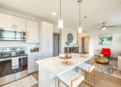Thumbnail 5 of 23 - Pet Friendly Apartments in Daytona Beach, FL - Madison Pointe - Designer Kitchen With Modern Cabinetry, Stainless Steel Appliances, Wood-Style Plank Flooring, Breakfast Bar with Bar-Style Chairs, Quartz Countertops, Designer Pendant Lighting, and View of Living Room