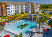 Thumbnail 1 of 23 - 3-BR Apartments In Daytona Beach, FL - Madison Pointe - Birds Eye View Of Pool With Center Island, Tables, Chairs, Umbrella, Lounge Beds, And Palm Trees.