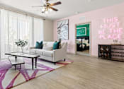 Thumbnail 19 of 27 - Luxury Apartments Near International Plaza in Tampa, FL - Mosaic Westshore - A bright living room with a pink accent wall featuring a neon sign, a white sofa, and a large purple-patterned rug.