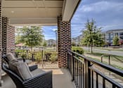 Thumbnail 34 of 53 - A balcony with a black chair and pillow is overlooking a green lawn.