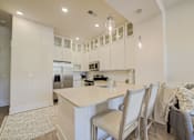 Thumbnail 21 of 53 - A kitchen with white cabinets and a large island with chairs around it.