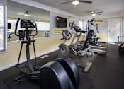 Thumbnail 29 of 30 - A gym with treadmills, elliptical machines, and a fan.