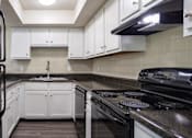Thumbnail 2 of 28 - A black refrigerator is in a kitchen with white cabinets.