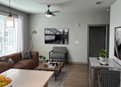Thumbnail 13 of 27 - A living room with a brown couch, a coffee table, and a ceiling fan.