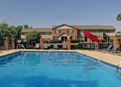 Thumbnail 1 of 23 - A swimming pool in front of a brick building with a red umbrella.