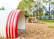 Thumbnail 23 of 31 - A red and white striped tunnel sits in a field of gravel.