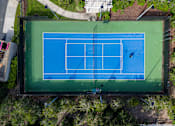Thumbnail 21 of 31 - A tennis court is surrounded by trees and has a green border.