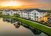 Thumbnail 36 of 45 - A sunset view of a white apartment complex reflected in a body of water.