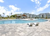 Thumbnail 34 of 48 - A large swimming pool surrounded by white lounge chairs and a building in the background.