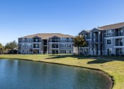 Thumbnail 32 of 33 - an apartment building overlooks a pond in front of a grass field  at Orion Prosper, Prosper, TX