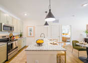 Thumbnail 8 of 40 - One-Bedroom Apartments in Athens, GA - Classic City Flats - Designer-Inspired Kitchen with Wood-Style Vinyl Plank Flooring, Rug, Granite Countertops, Stainless Steel Appliances, Tan Cabinetry, Island/Breakfast Bar with Seating, Pendant Lights, and View of Dining Area and Bedroom.