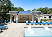 Thumbnail 29 of 33 - A pool pavilion with a blue roof and white walls is surrounded by blue lounge chairs.