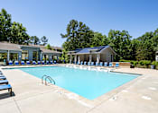 Thumbnail 28 of 33 - A large swimming pool with sun loungers and a building in the background.
