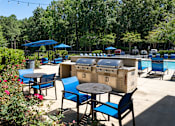 Thumbnail 30 of 33 - A patio with blue chairs and tables is surrounded by greenery.