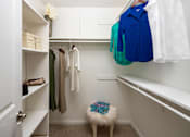 Thumbnail 20 of 33 - A white closet with clothes hanging and a stool in front.