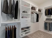 Thumbnail 26 of 43 - A walk in closet with clothes hanging and shelves.