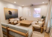 Thumbnail 9 of 36 - A modern living room with a large painting on the wall and a seating area with a sofa and chairs.