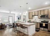 Thumbnail 1 of 24 - Dog-Friendly Luxury Apartments in Flagler Beach, FL - Preserve at Flagler Beach - Kitchen with Wood-Inspired Flooring, Kitchen Island with Seating, Pendant Lighting, Granite Countertops, Stainless-Steel Appliances, Wood-Tone Cabinetry, and View of Living Area.