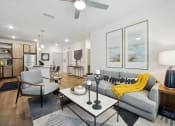 Thumbnail 3 of 24 - Flagler Beach, FL, Pet-Friendly Luxury Apartments - Preserve at Flagler Beach - Living Room with Wood-Inspired Flooring, Area Rug, Couch, Armchair, Coffee Table, Side Table with Lamp, Ceiling Fan, and View of Kitchen Area.