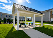 Thumbnail 60 of 65 - A pavilion with a white roof and blue benches is situated in a grassy area.