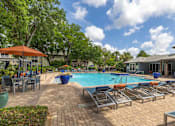 Thumbnail 3 of 31 - A pool area with sun loungers and a building in the background.