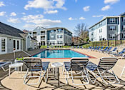 Thumbnail 4 of 13 - A pool surrounded by chairs and tables in front of apartment buildings.