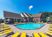 Thumbnail 15 of 25 - Fully Furnished Apartments in Johnson City, TN - University Edge - Resort-Style Swimming Pool With Large Sundeck, Yellow Lounge Chairs, Patio Umbrellas, And Brick Clubhouse Under Blue Sky.