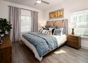 Thumbnail 13 of 27 - Pet-Friendly Luxury Apartments in Ridgeville, SC - Preserve at Ridgeville - Bedroom With Upholstered Bed, Blue Bedding, Wooden Nightstand With Lamp, Two Large Windows With Curtains And Blinds.