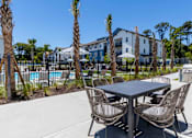 Thumbnail 24 of 40 - A table and chairs set up outside with palm trees and apartment buildings in the background.