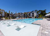Thumbnail 28 of 40 - A large swimming pool with sun loungers and a building in the background.