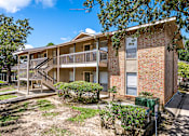 Thumbnail 27 of 30 - A two-story brick apartment building with a balcony and a small garden in front.