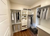 Thumbnail 16 of 32 - A walk in closet with clothes hanging and shelves.