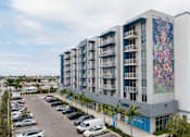 Thumbnail 34 of 35 - A large building with a mural on the side is surrounded by a parking lot.