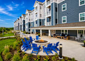Thumbnail 25 of 30 - A large building with a blue and white exterior and a patio with blue chairs and a fire pit.