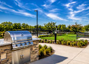 Thumbnail 24 of 30 - A BBQ grill is on a patio with a fence and trees in the background.