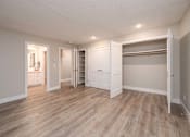 Thumbnail 24 of 48 - Dog-Friendly Apartments in North Bellevue, WA - The Regent at Bellevue Way - An Empty Bedroom with Wood Plank Flooring, Wardrobe with Shelves, Closet with Rod, and a Doorway Leading to the Bathroom.